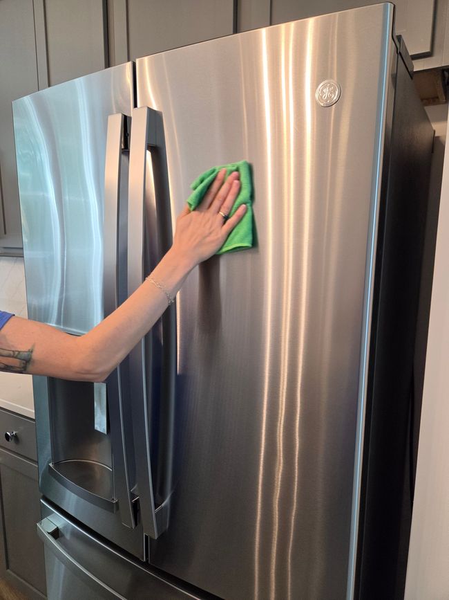 Hand wiping a stainless steel refrigerator with a green cloth