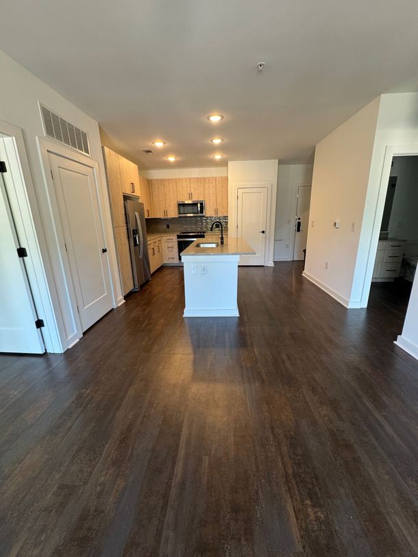 Open-concept kitchen and living area with dark wood floors, white cabinets, and a small island.