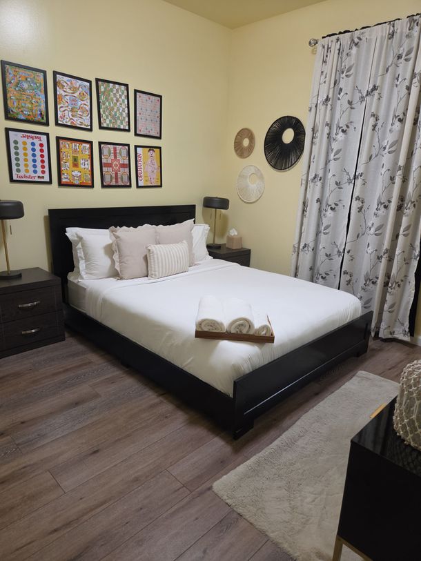 Cozy bedroom with a neatly made white bed, framed wall art, and patterned curtains.