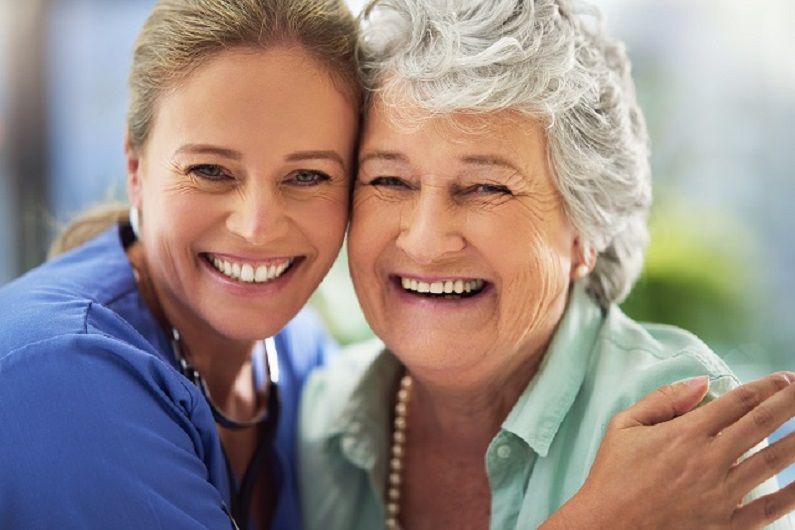a nurse is hugging an older woman and they are smiling for the camera .
