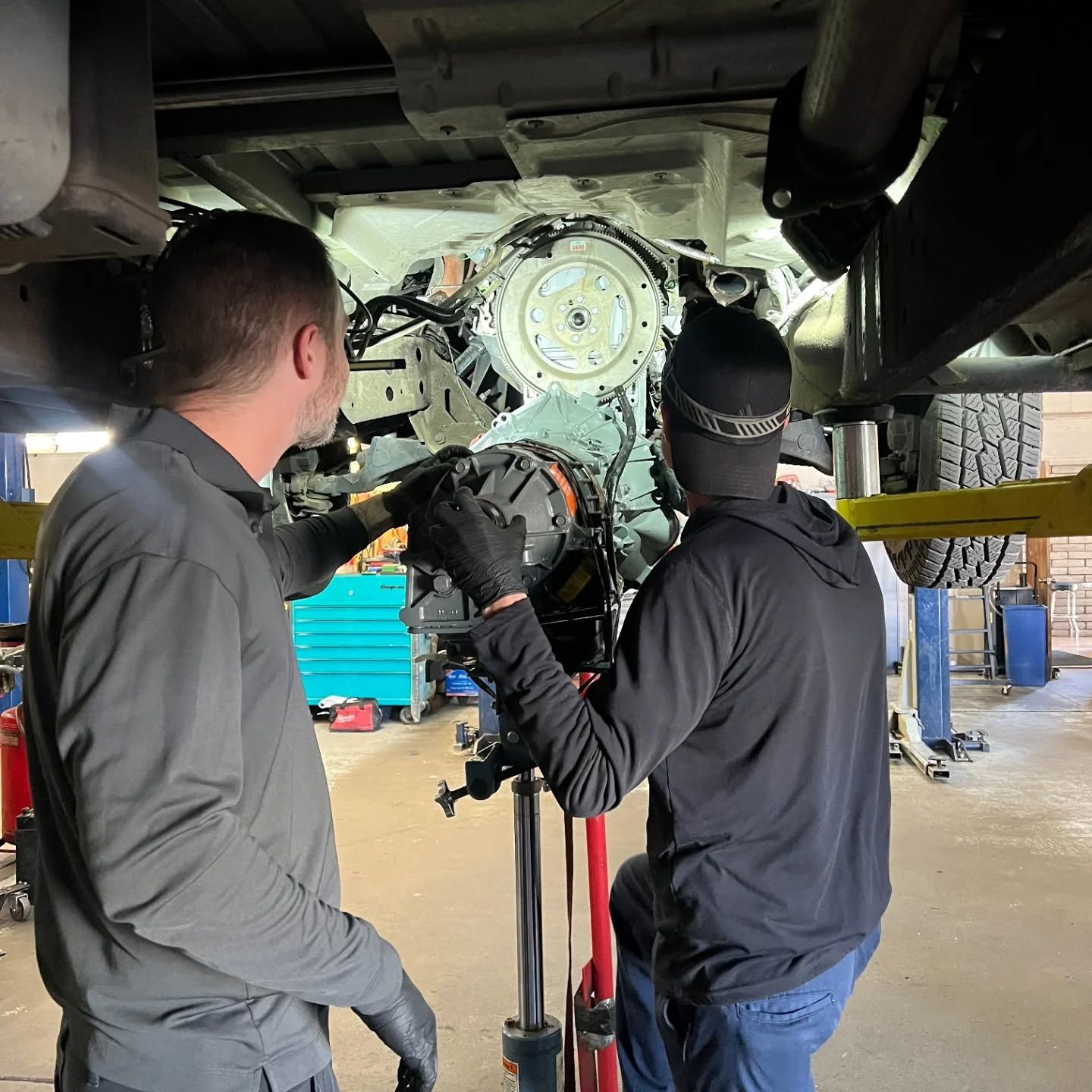 Two mechanics inspect an engine under a lifted vehicle in a garage | Flagstaff Auto Repair