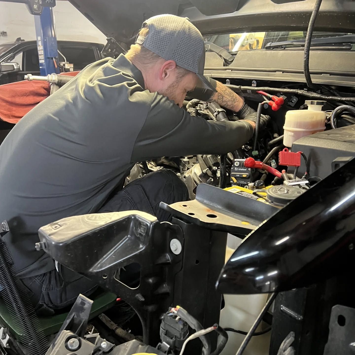Mechanic leaning into an open vehicle engine bay, working on wiring in a garage. | Flagstaff Auto Repair