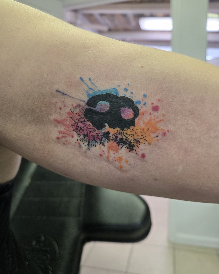 Tattoo on an arm, featuring a black shape with colorful paint splatter effect.