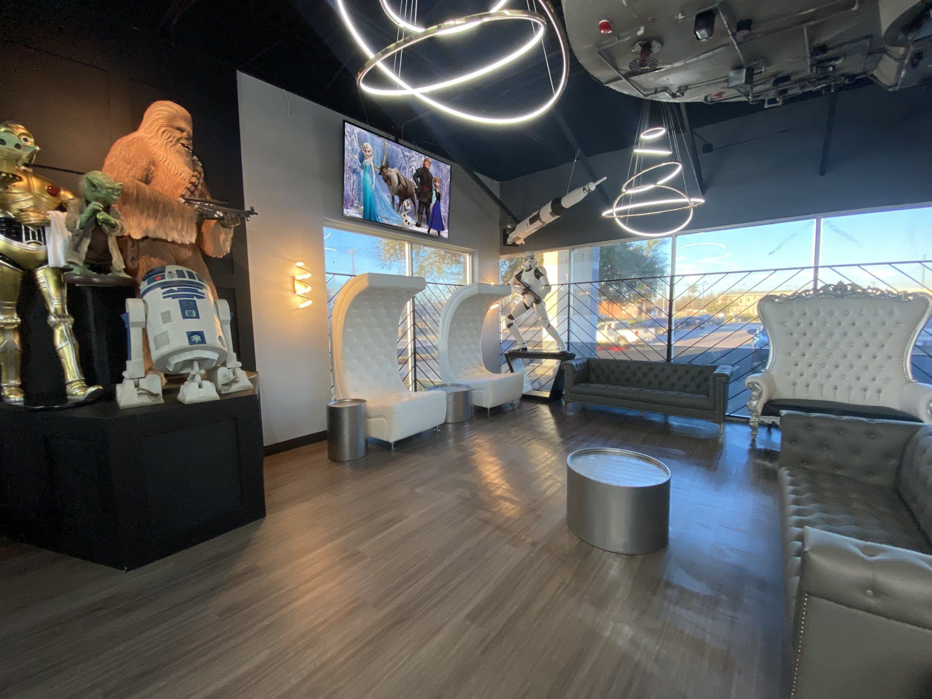 Lounge with Star Wars figures on a platform, modern white chairs, gray sofas, a round coffee table, and circular lights.