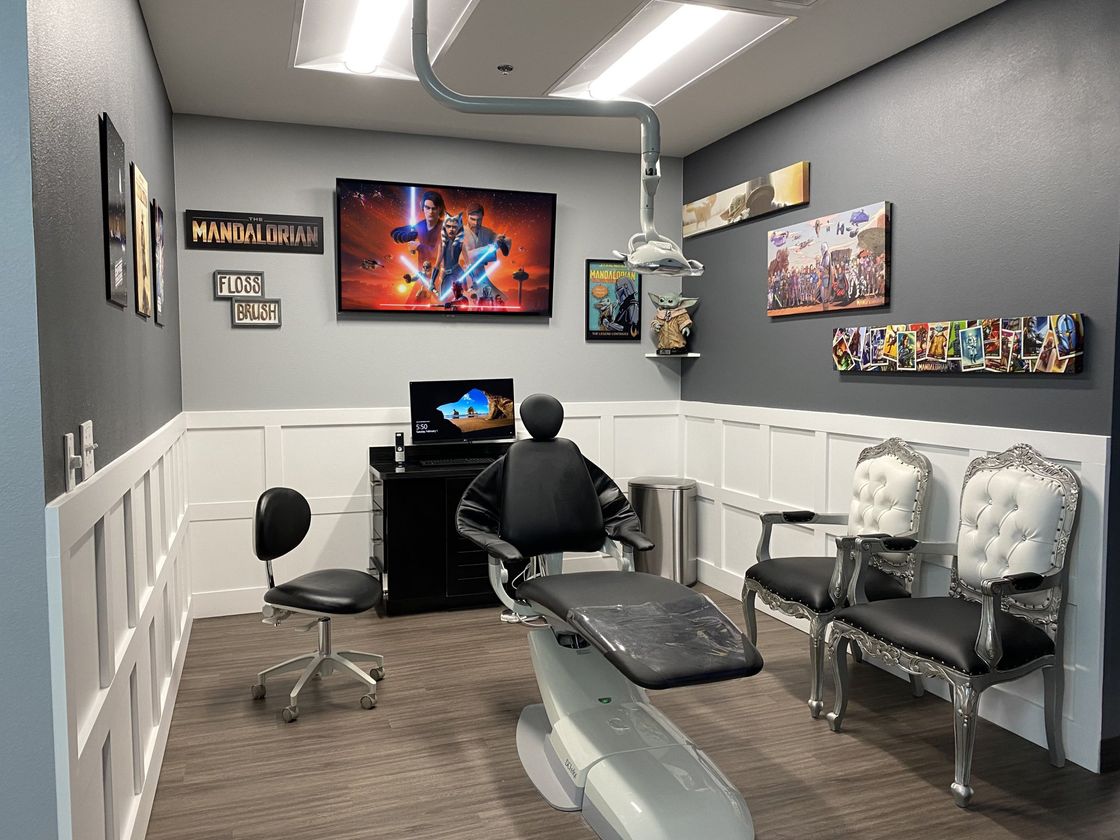 A modern dental or medical office featuring a reclining chair, exam stool, and two decorative chairs against gray walls.
