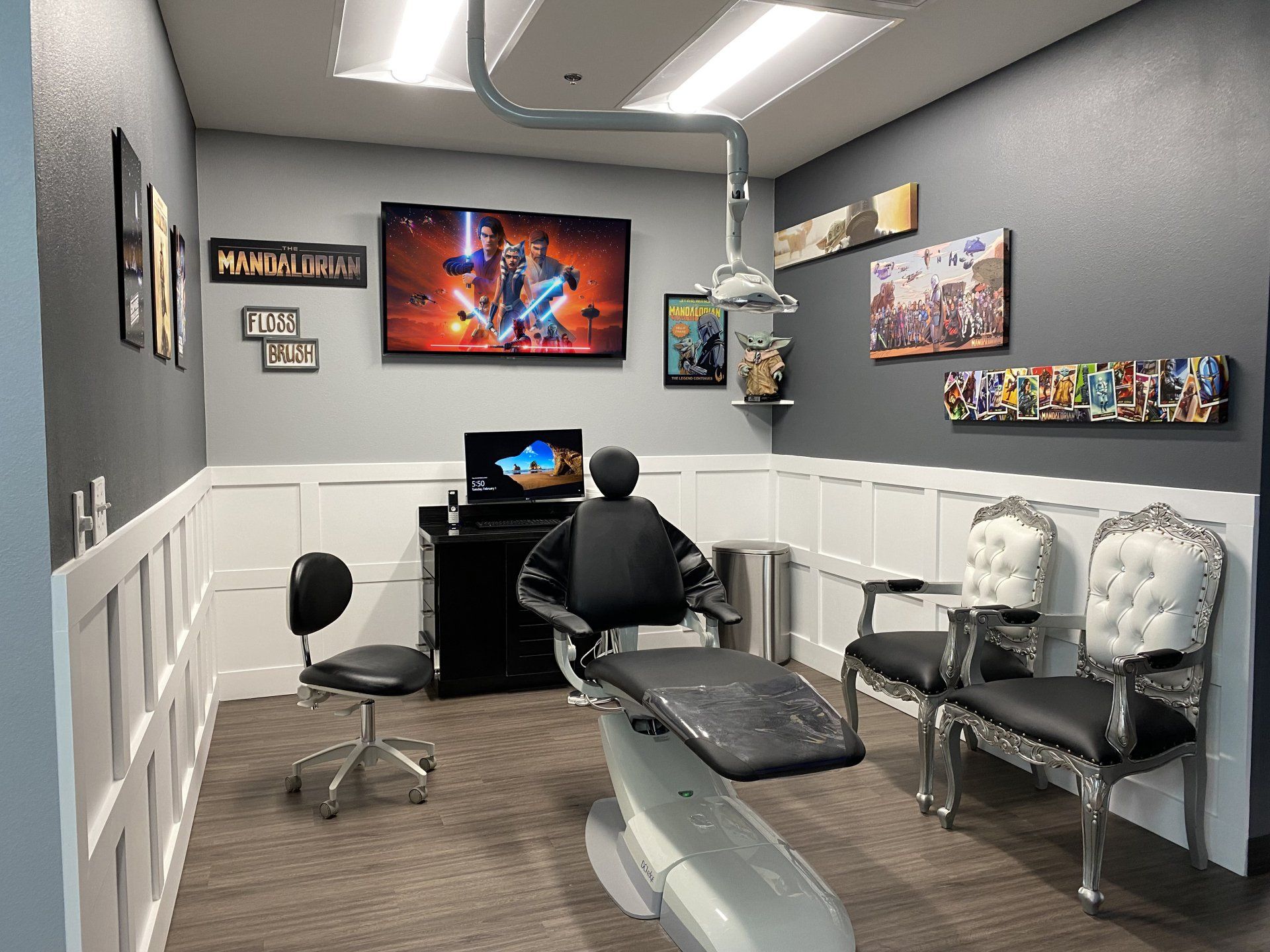 A modern medical or dental exam room with a central black chair, computer station, and two ornate white chairs.
