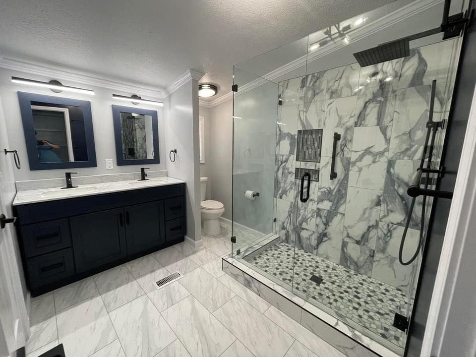 Modern bathroom with navy vanity, marble shower, and gray tile flooring.