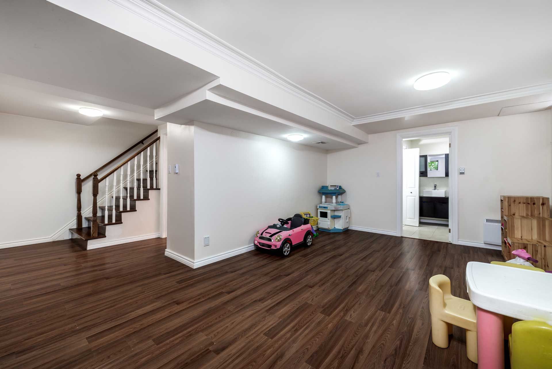 Basement play area with wood floors, pink car, play kitchen, and white walls