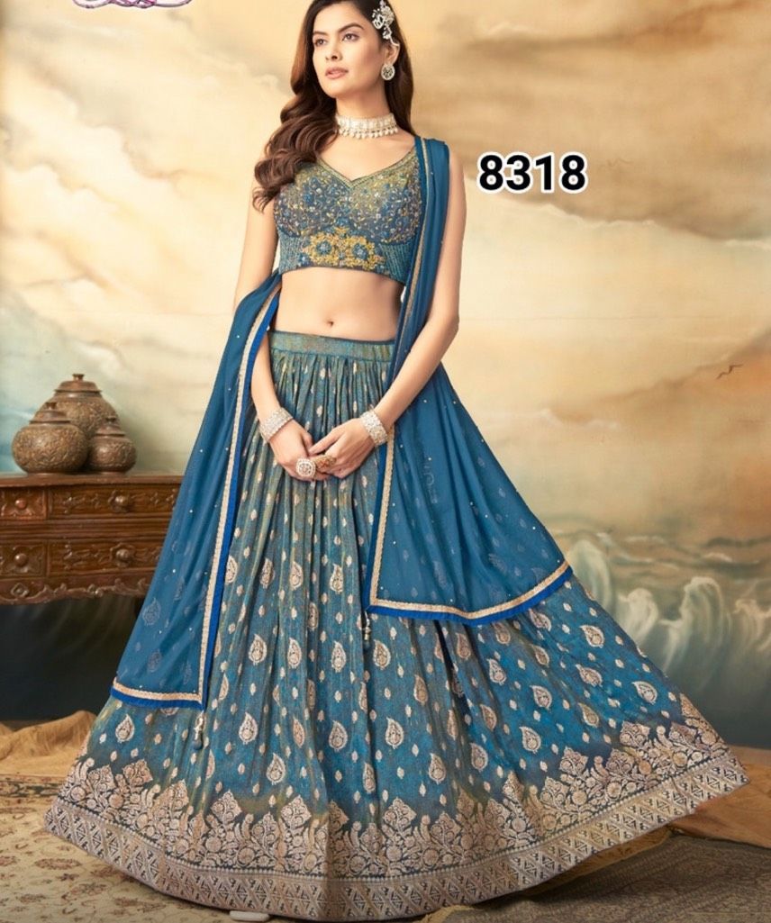 Woman in a blue and gold embroidered lehenga, standing indoors. She's wearing a crop top and a dupatta.