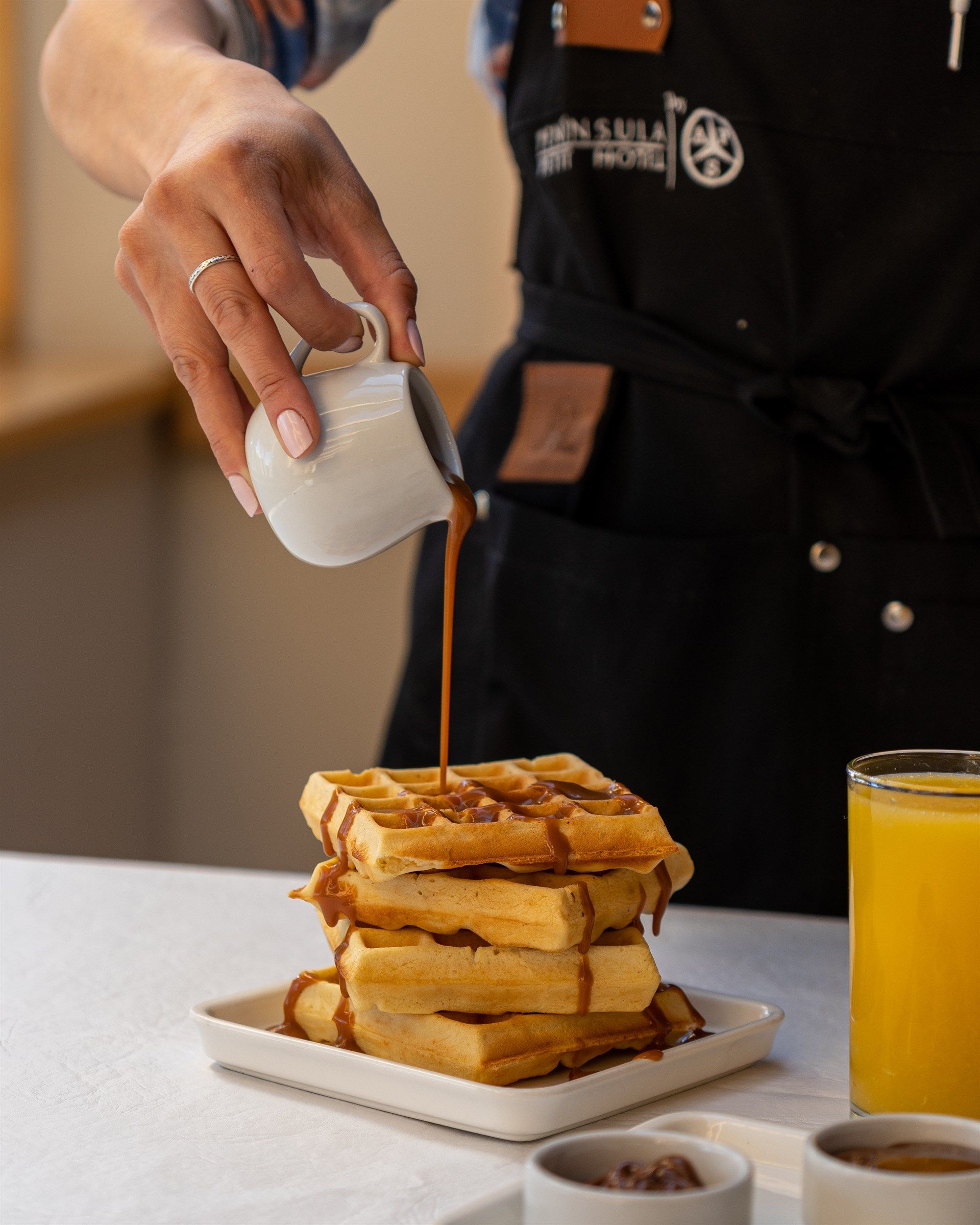 Una persona está vertiendo jarabe sobre una pila de waffles.