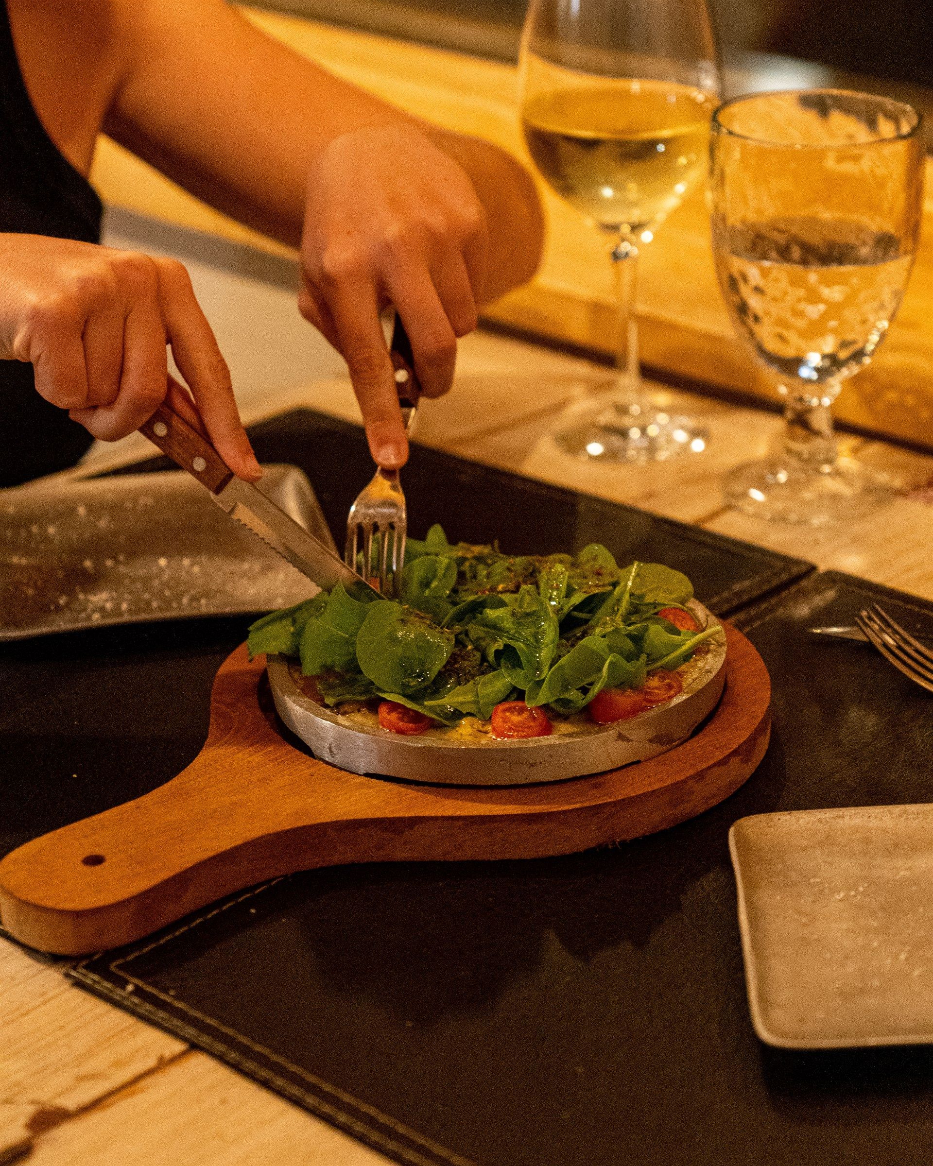 Una persona está cortando una pizza en una tabla de cortar de madera.