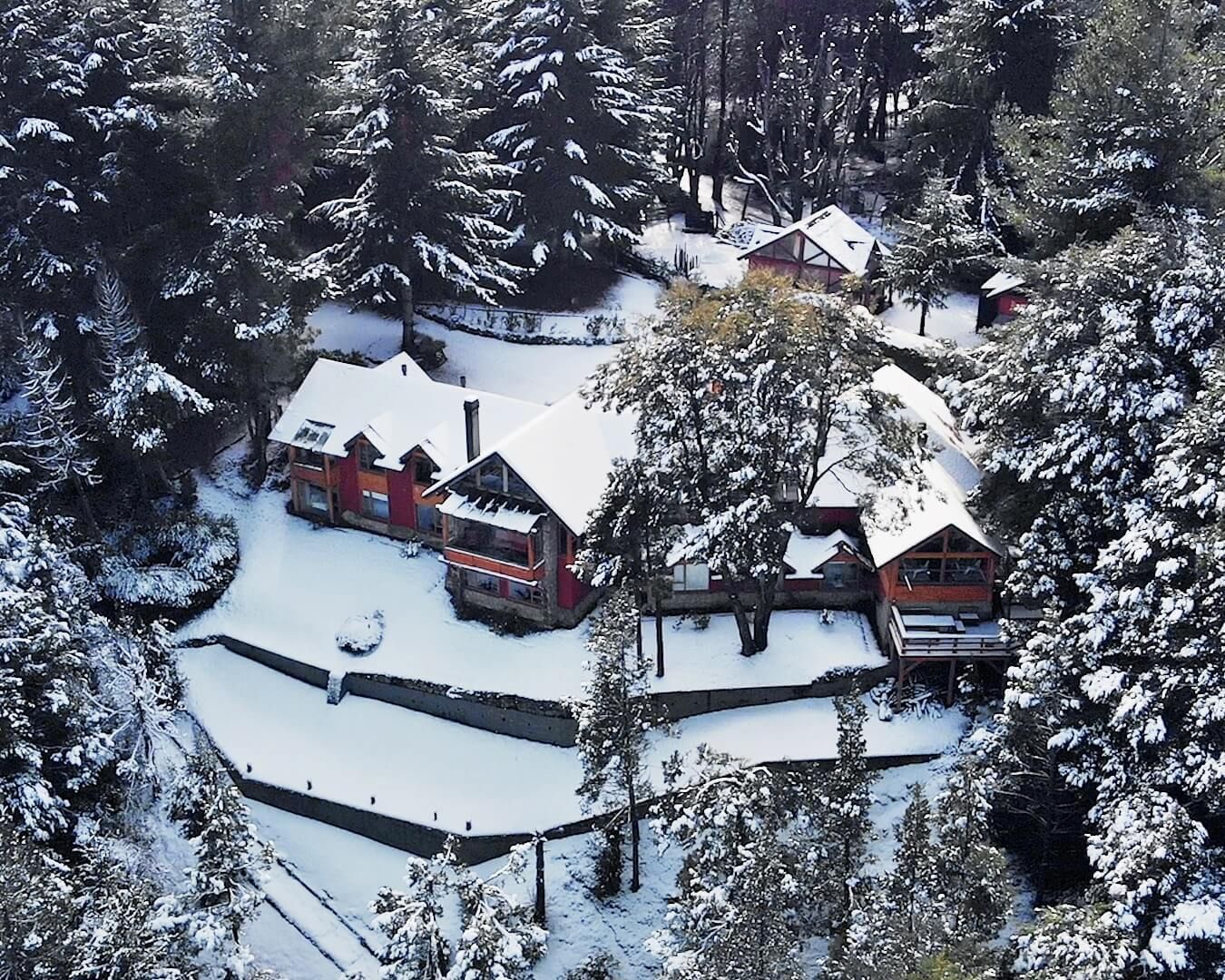 Una vista aérea de una casa rodeada de árboles cubiertos de nieve.