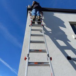 A man is standing on a ladder on the side of a building.