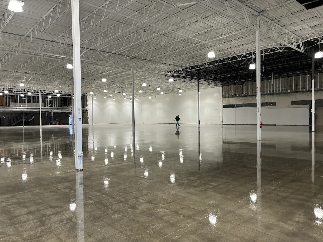Empty warehouse interior with polished concrete floor, bright overhead lights, and a lone person in the distance