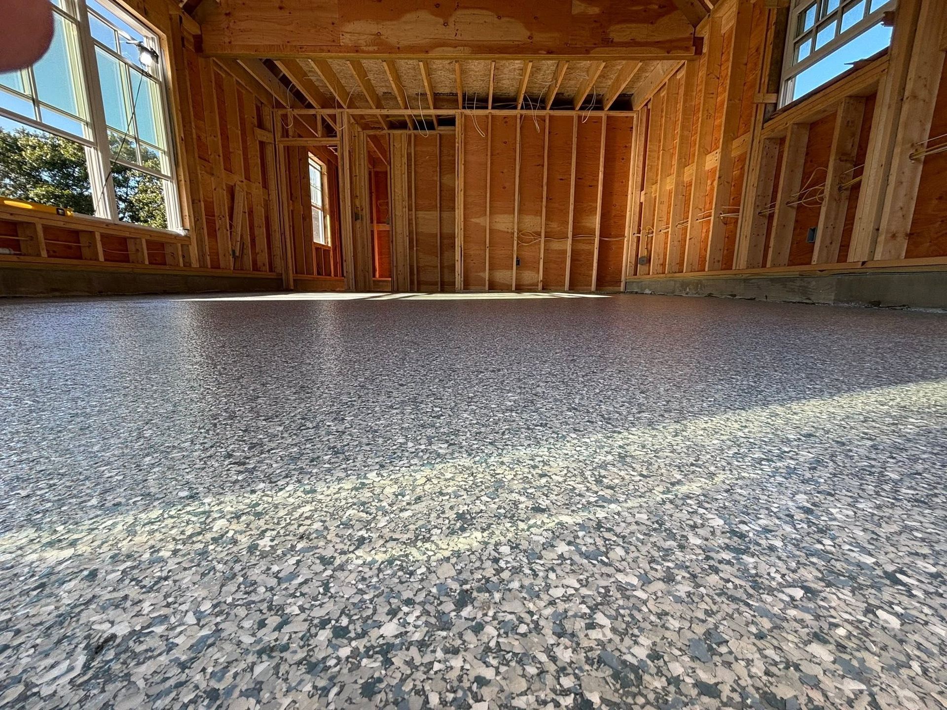 Unfinished wooden house interior with exposed framing and a speckled epoxy floor