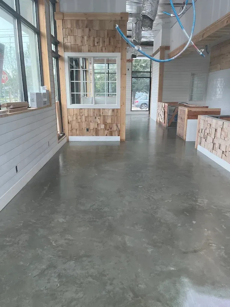Empty interior space with polished concrete floor, wood-paneled walls, and large windows under construction details