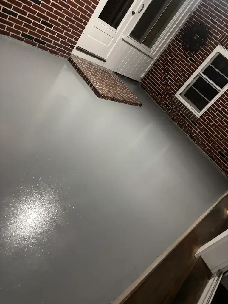 Empty gray concrete porch outside a brick house with a white door and window.