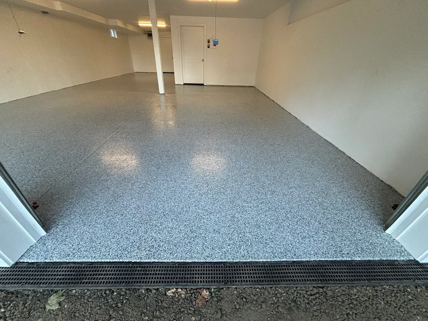 Empty indoor garage with speckled floor and white walls, viewed from an open doorway