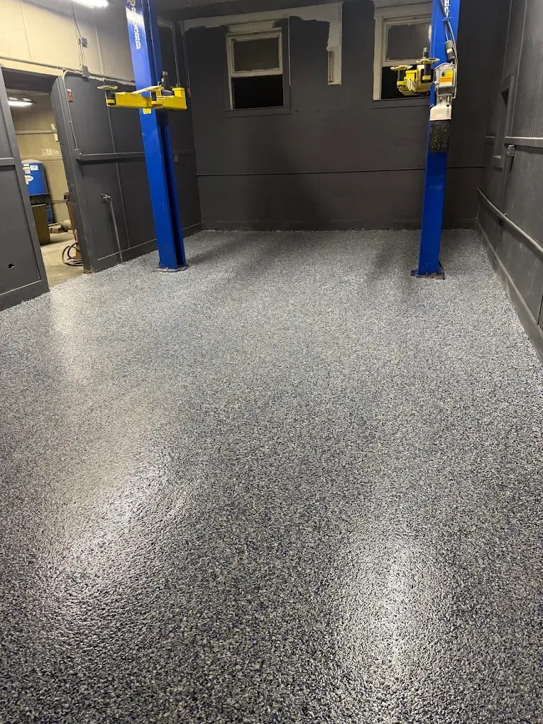 Empty gray room with speckled floor, two blue support posts, and a small window.