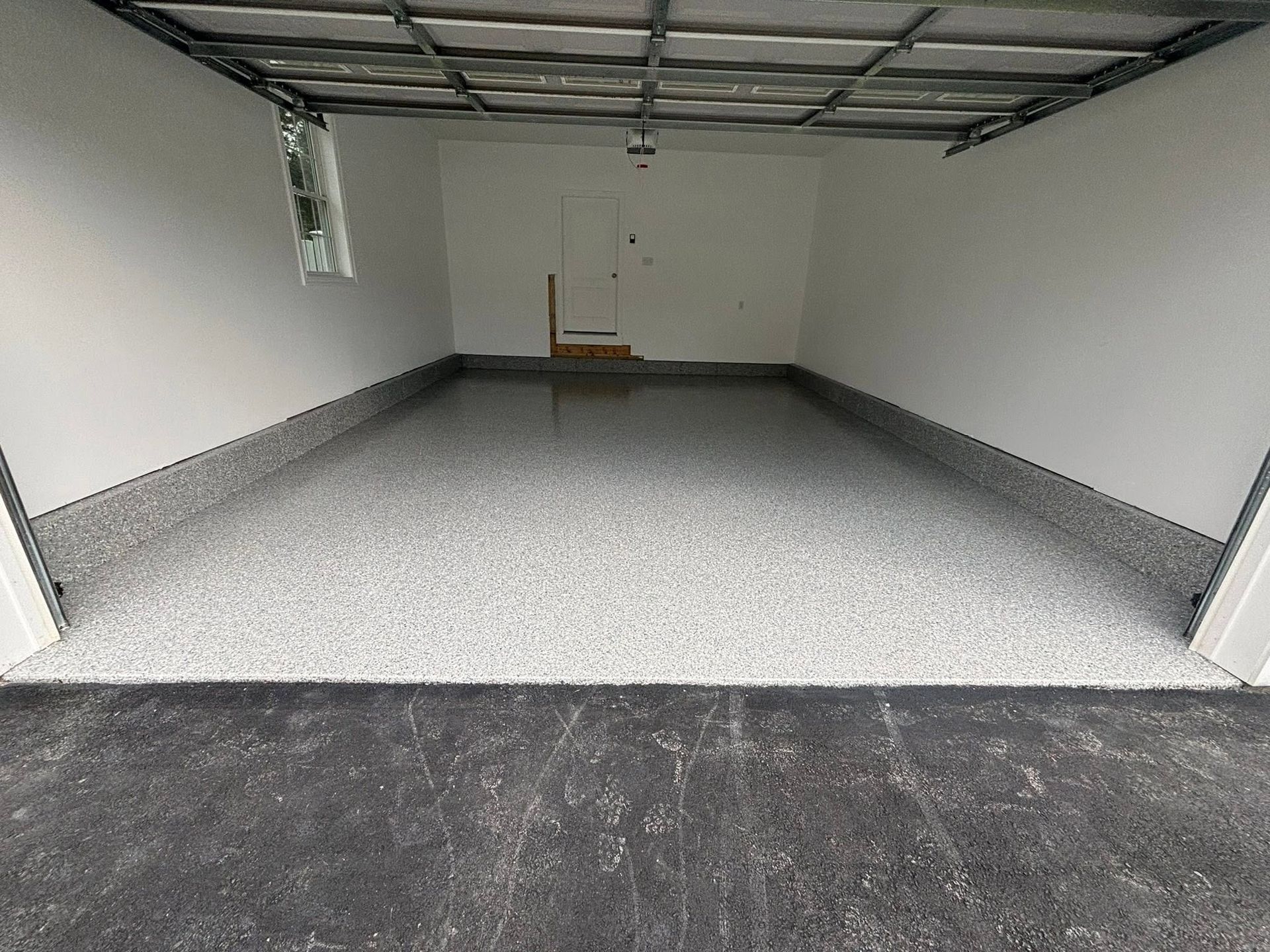 Empty unfinished garage with gray floor, white walls, and exposed ceiling beams
