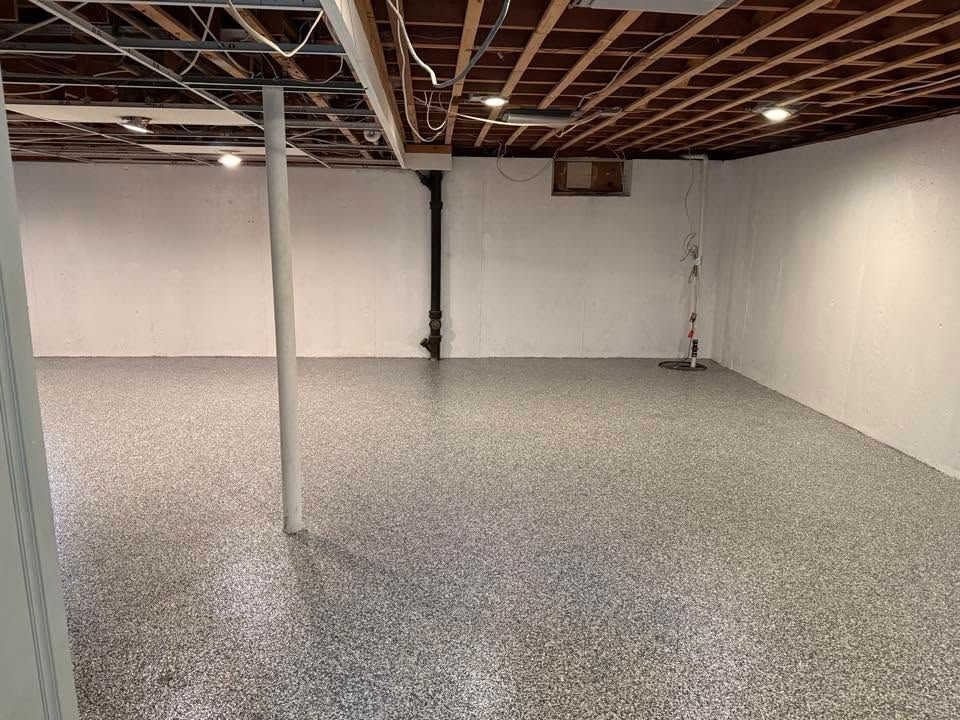 Empty basement with white walls, exposed ceiling joists, and a speckled gray floor