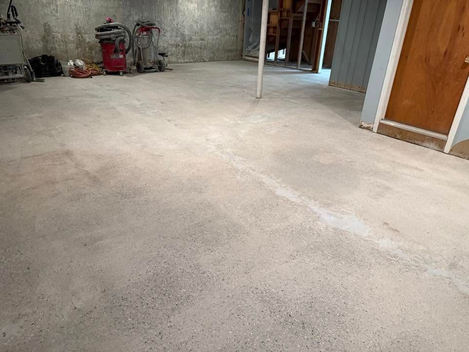 Empty unfinished room with bare concrete floor, white columns, and construction tools along the wall.