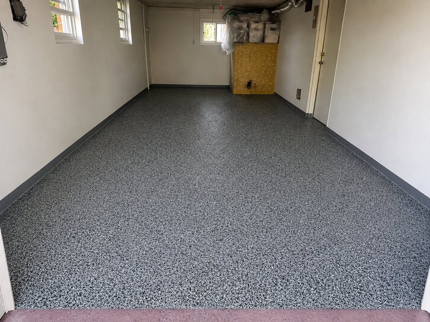 Empty carpeted room with gray speckled floor, white walls, and a small window at the back