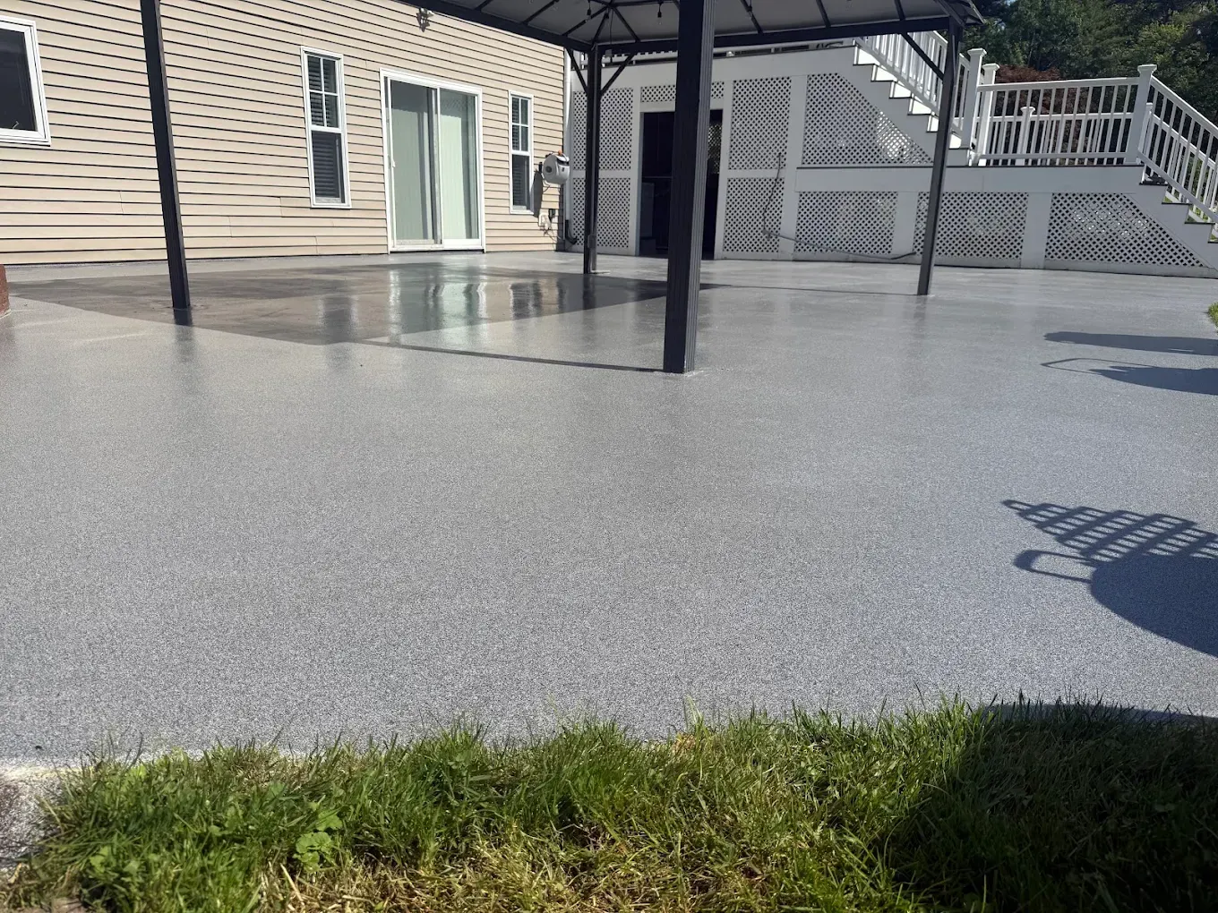 Outdoor patio with fresh gray concrete, black posts, and a beige house exterior.