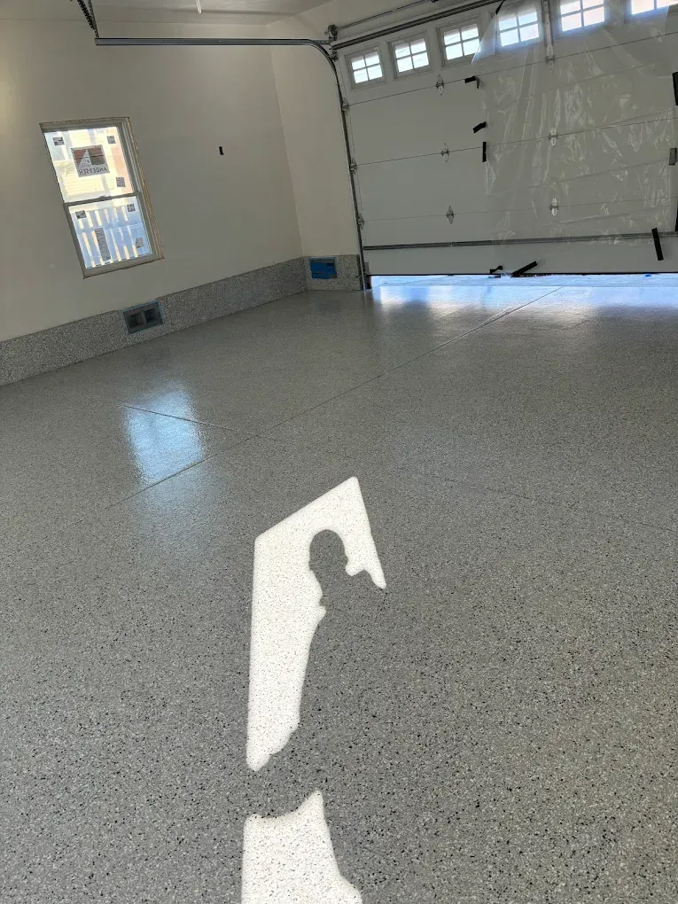 Empty garage with gray speckled floor, white walls, and a bright sunlit patch on the floor.