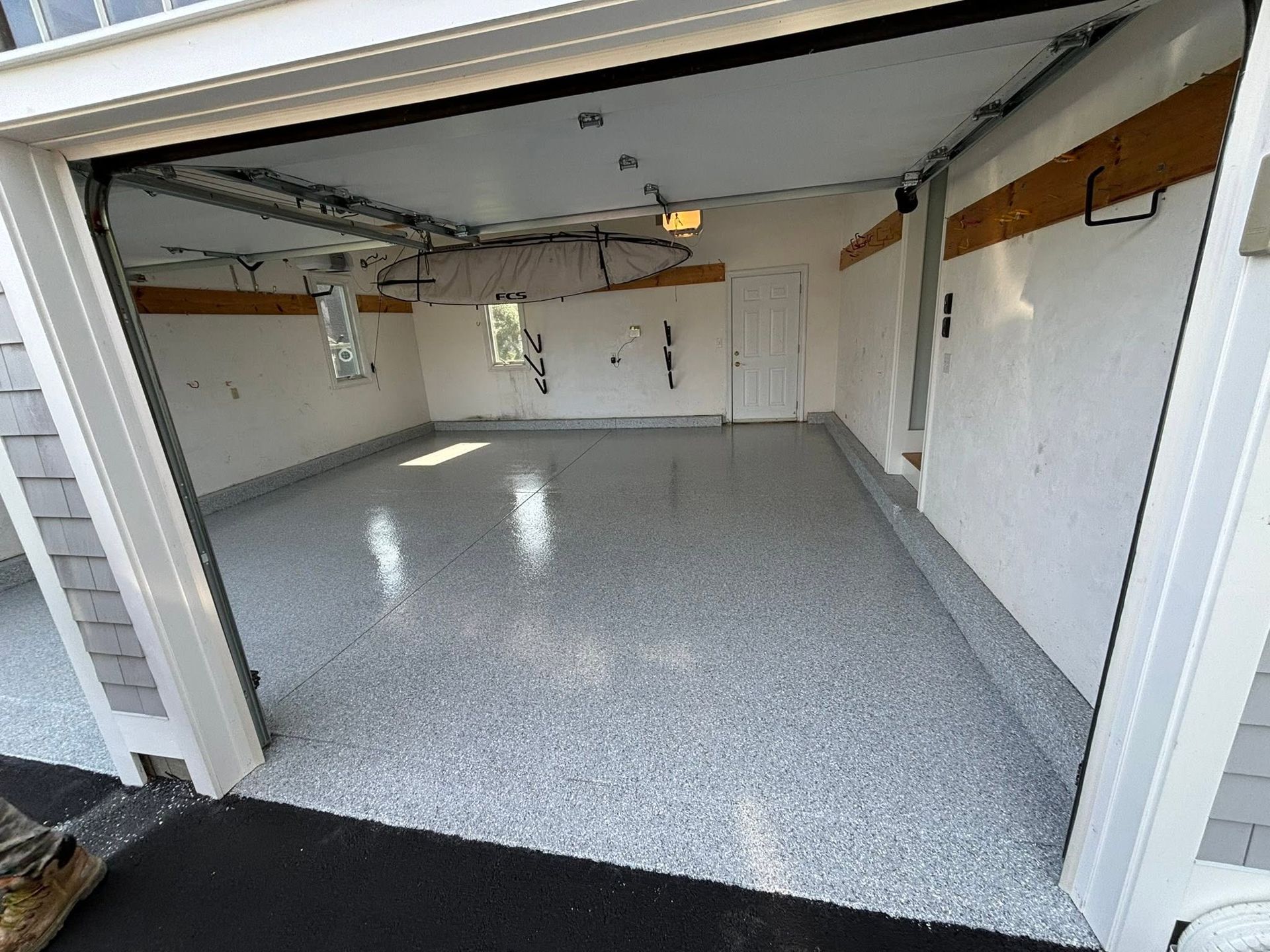 Empty garage with speckled epoxy floor and open door, viewed from inside.