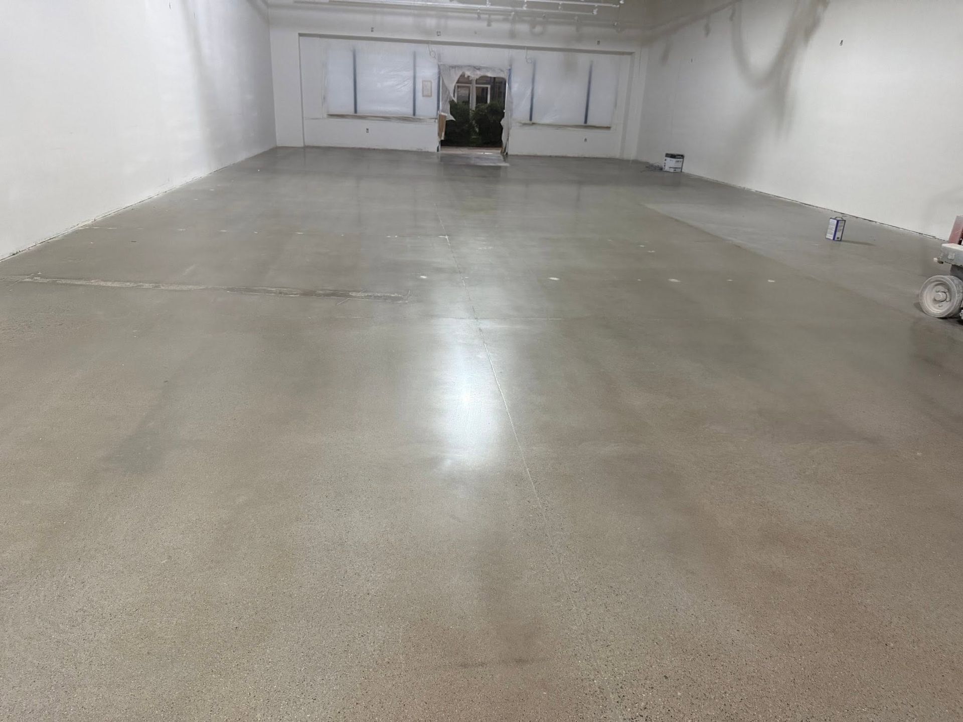 Empty white-walled warehouse with polished concrete floor and windows at the far end