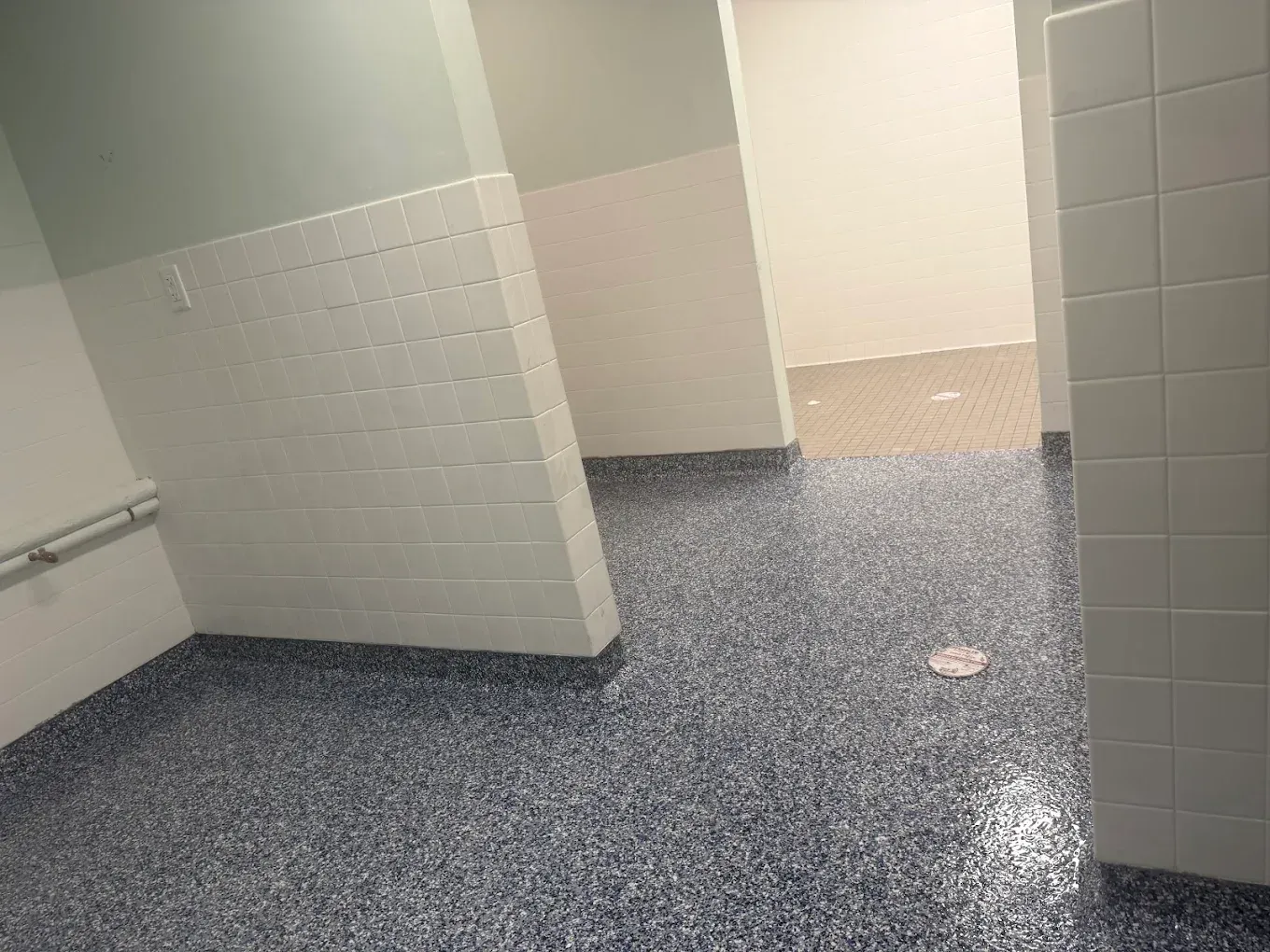 Empty public restroom with tiled stalls and blue-speckled floor, viewed through open stall doors