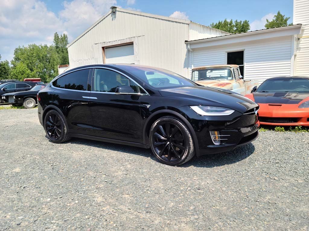 A black tesla model x is parked in a gravel lot.
