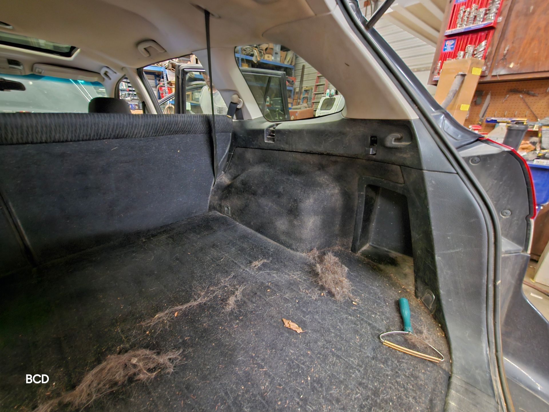 Dirty car interior, black upholstery, visible debris, tool present.