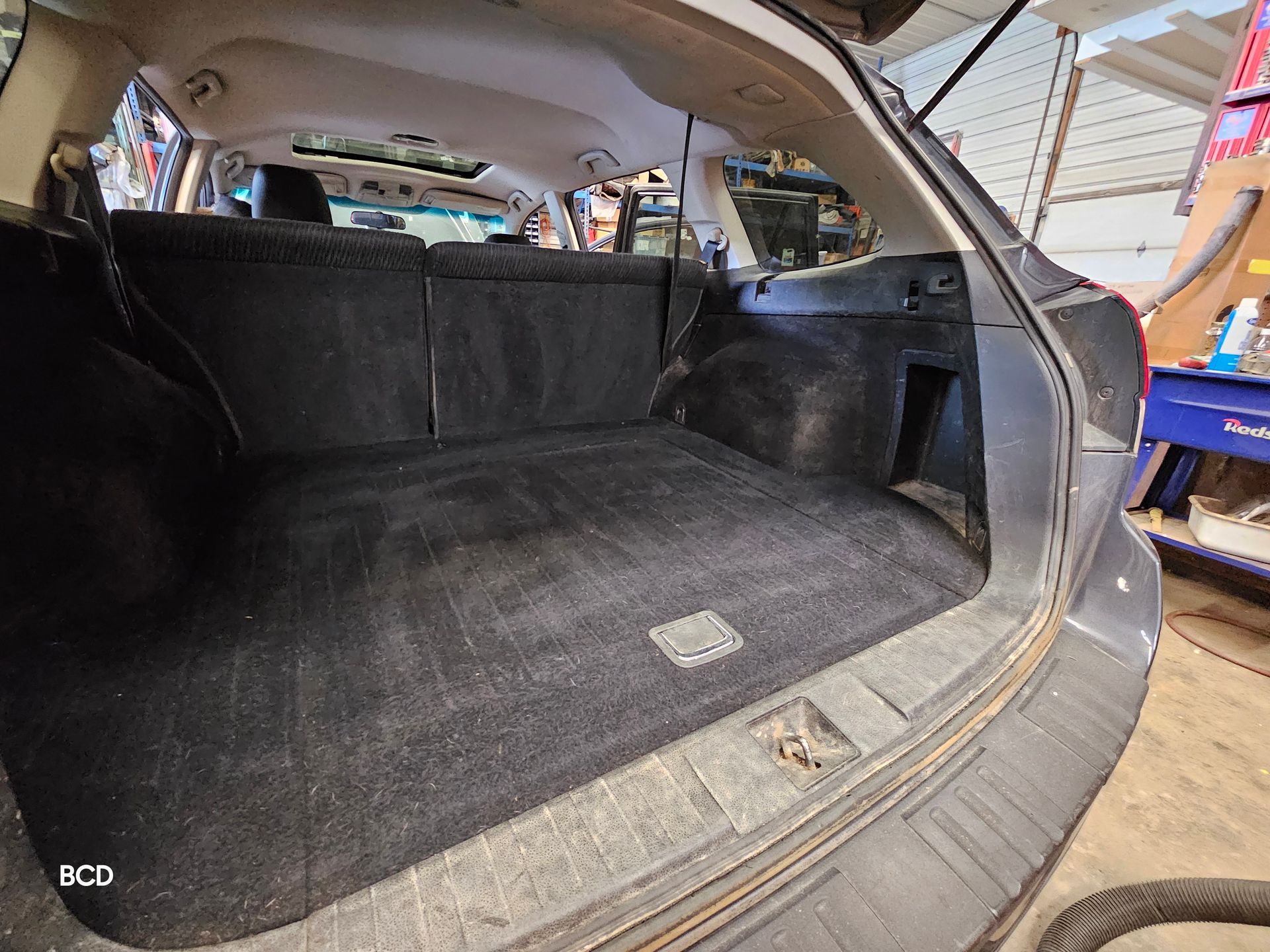 Black-carpeted cargo area of a gray car. The car is open, revealing a clean, empty space, ready for cargo.