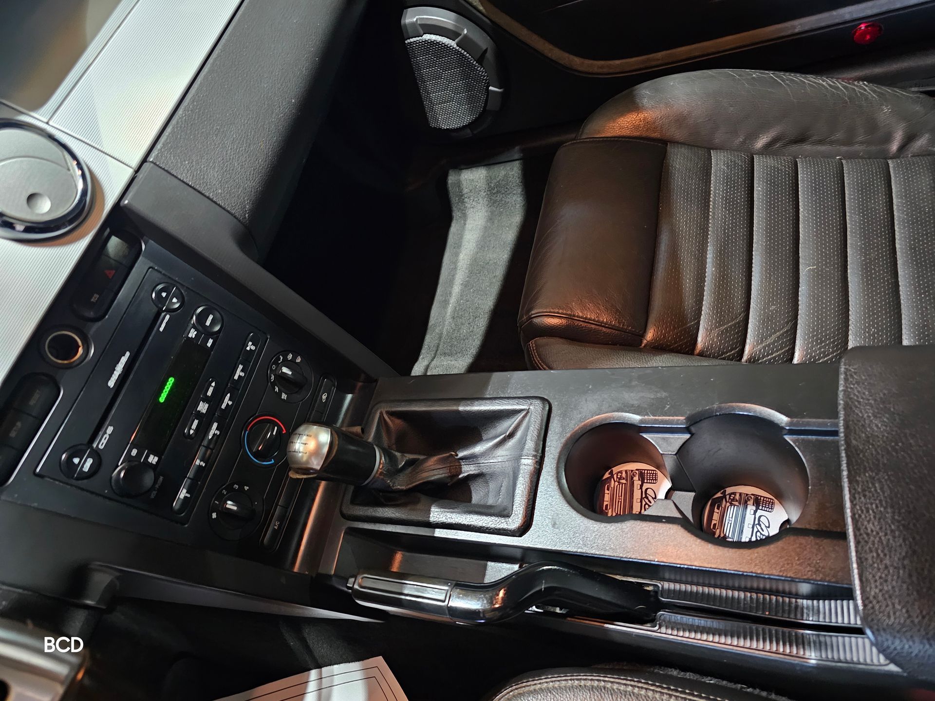 Interior view of a car, showing the center console with the gear shift, radio, and cup holders.
