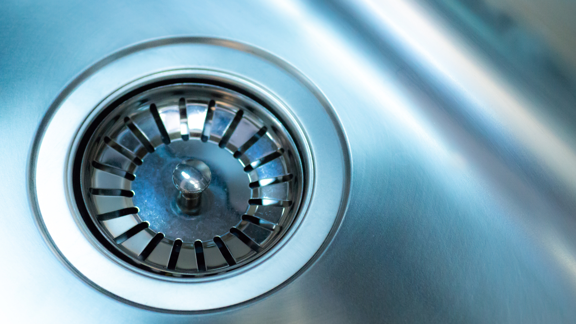 A close up of a drain in a stainless steel sink.