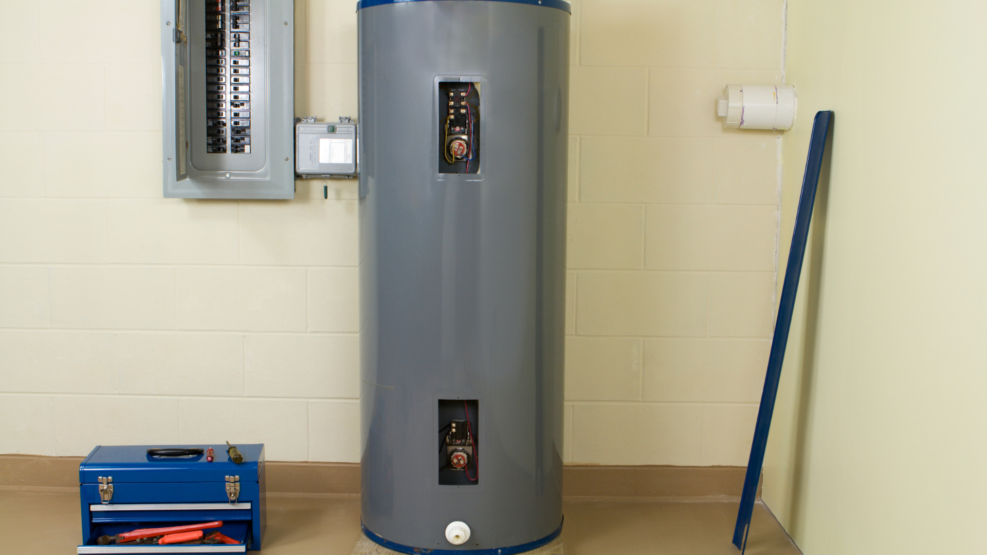 A water heater is sitting in a corner of a room next to a toolbox.