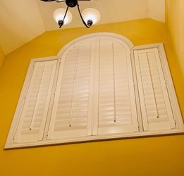 A chandelier is hanging from the ceiling above a window with shutters