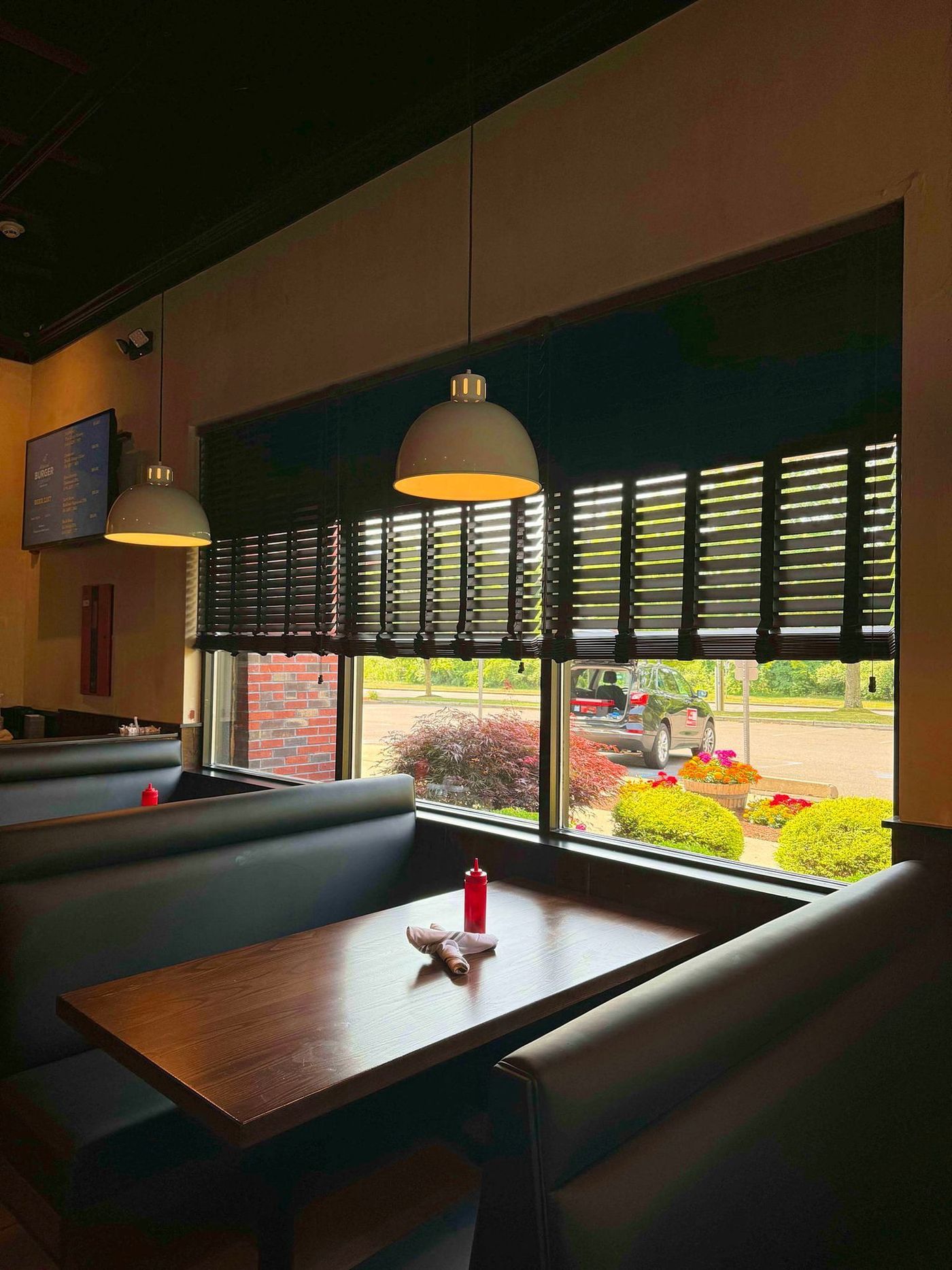 The inside of a restaurant with tables and benches and a large window.