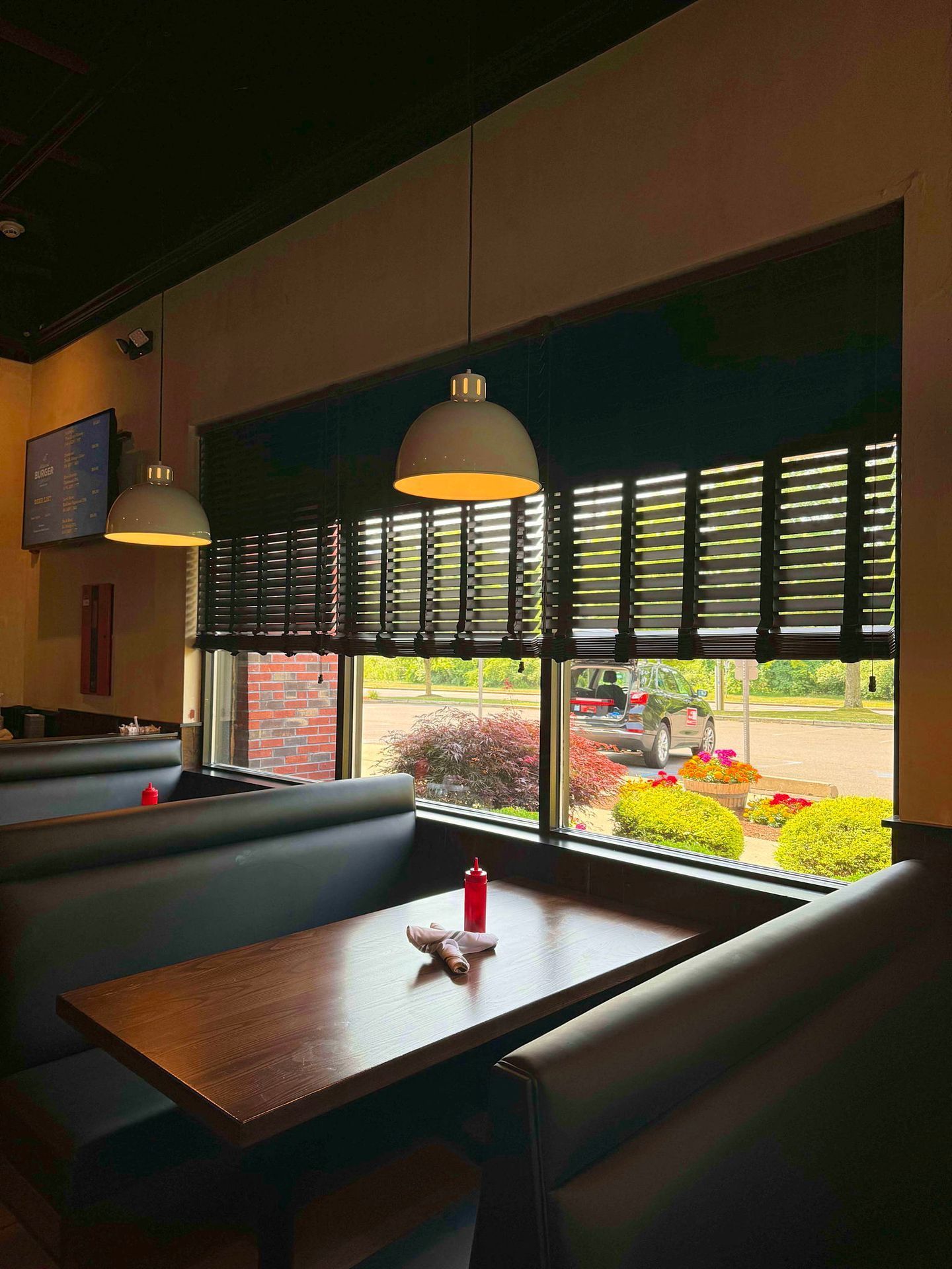 The inside of a restaurant with tables and benches and a large window.