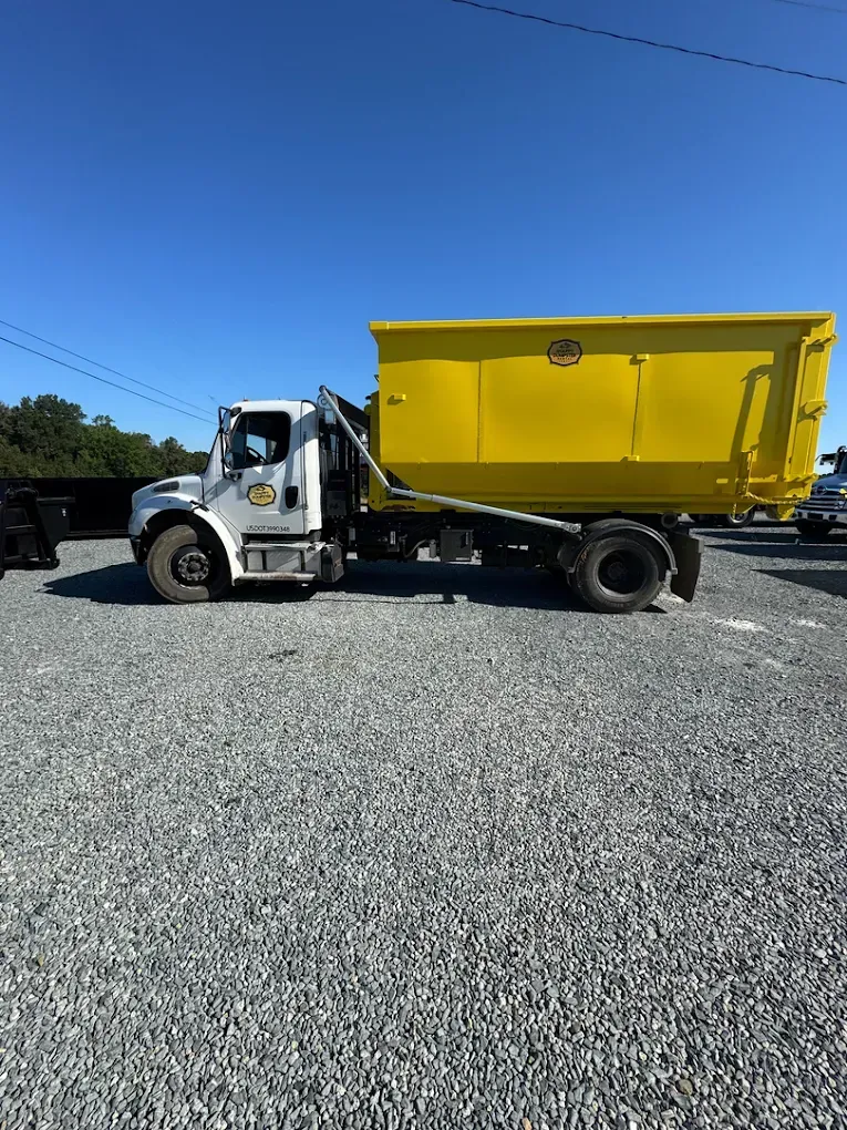 Yellow dump truck parked on a gravel lot under a clear blue sky
