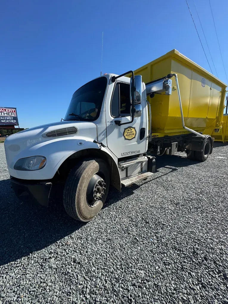White and yellow dump truck parked on gravel under a clear blue sky