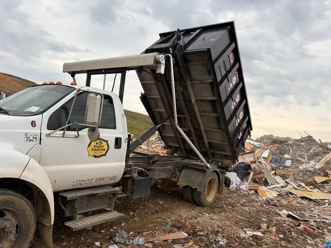 White roll-off hooklift truck unloading debris at a landfill under a cloudy sky