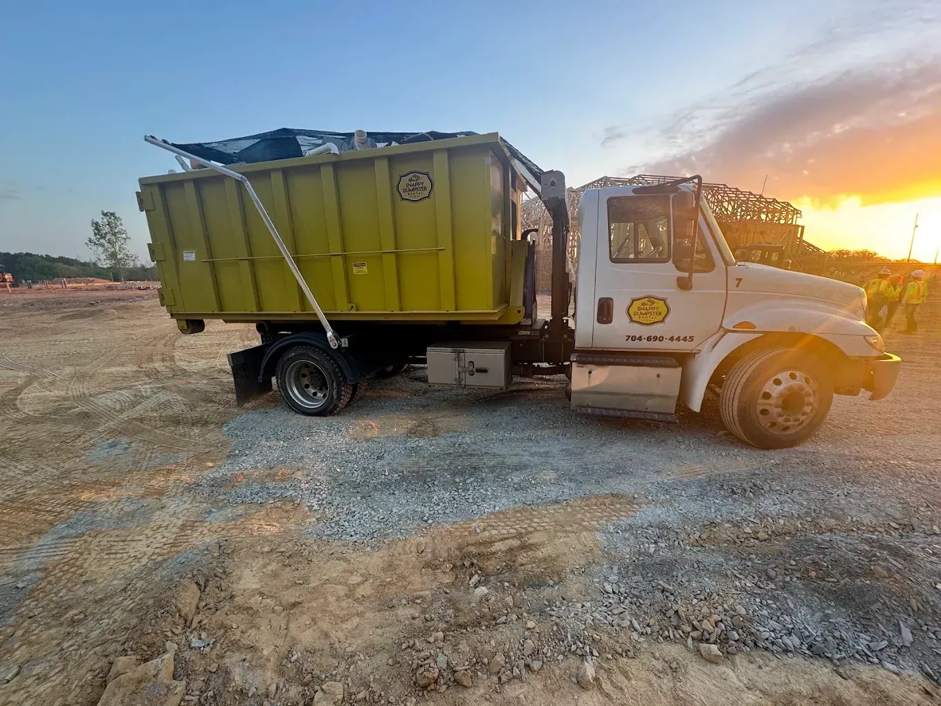 Yellow dump truck at sunset on a gravel lot, with a large yellow cargo bed.