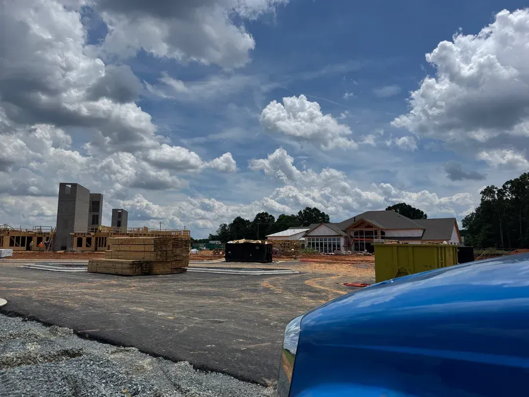 Construction site with unfinished buildings, stacked materials, and a blue vehicle under a cloudy sky