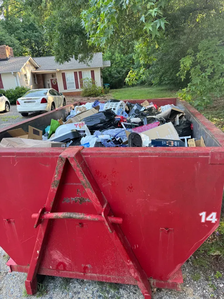 Red dumpster filled with trash in a residential driveway