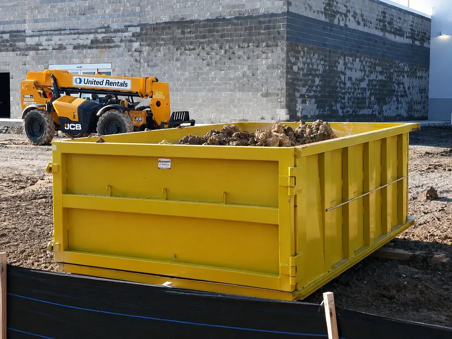 White and yellow dump truck parked on gravel under a clear blue sky
