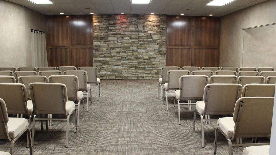 Chapel interior at Campbell-Aman Funeral Home with rows of padded seating facing a decorative stacked stone focal wall.