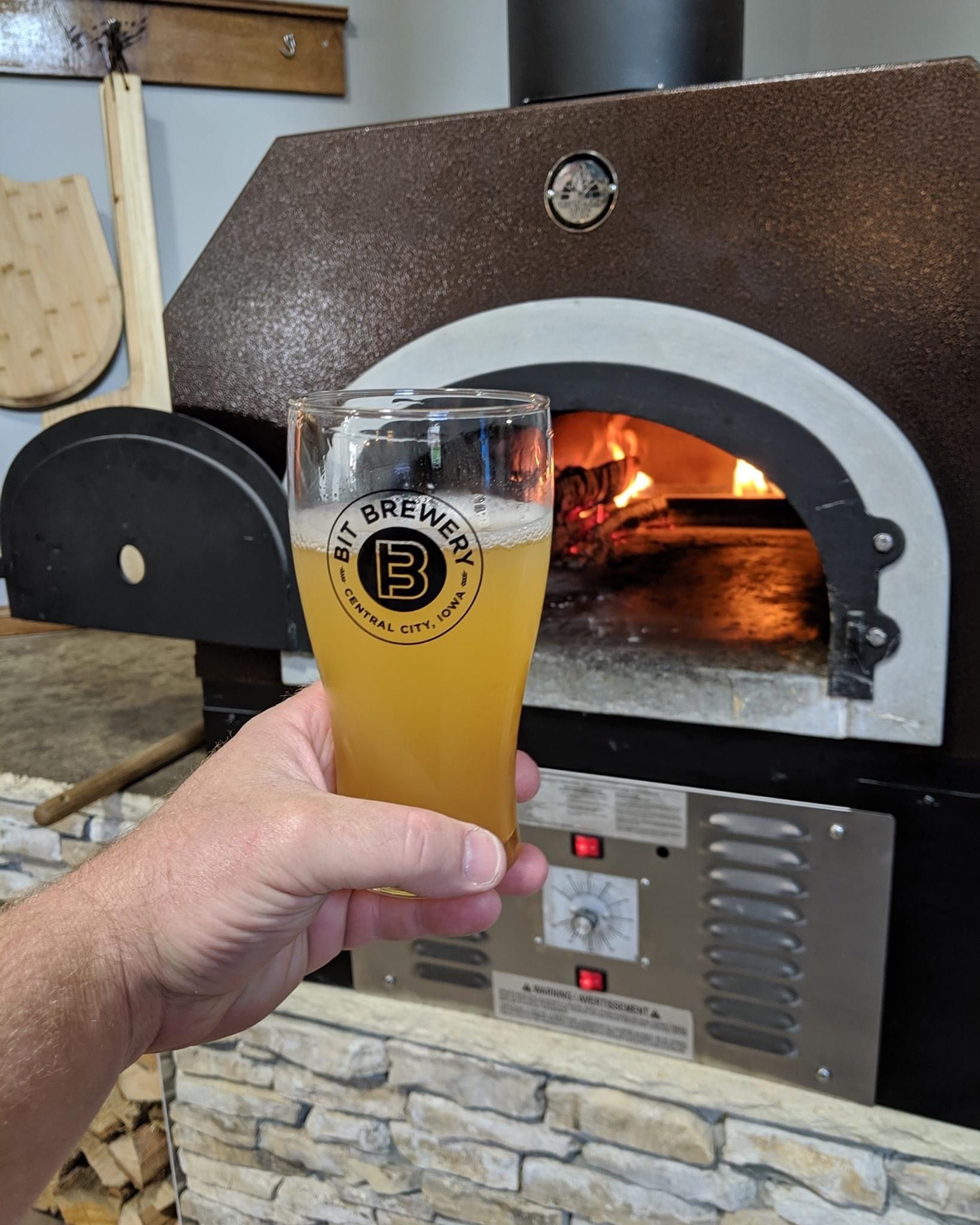 A person is holding a glass of beer in front of a pizza oven.